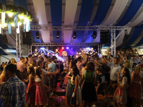 Menschen tanzen und feiern auf einem Volksfest mit einer Live-Band im Hintergrund.