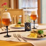 Ein Teller mit gegrilltem Fisch, Beilagen und zwei Gläsern Bier auf einem Tisch.