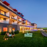 Außenansicht eines modernen Hotels mit Pool und Liegen in einem Gartenbereich bei Dämmerung.