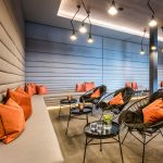 Moderne Lounge mit grauen Wänden, orangefarbenen Kissen und stilvollen Lampen an der Decke.