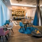 Moderne Lounge mit mehreren Tischen, Stühlen und einem offenen Kamin in einem stilvollen Raum.