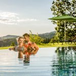 Ein Paar steht im Pool und hält Cocktails in der Hand, umgeben von Natur.