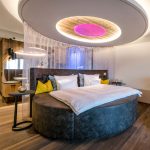 Rundes Bett mit Kissen und einem beleuchteten Deckenpaneel in einem modernen Schlafzimmer.