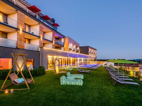 Ansicht des Hüttenhof Hotels mit Garten und Liegen bei Dämmerung.