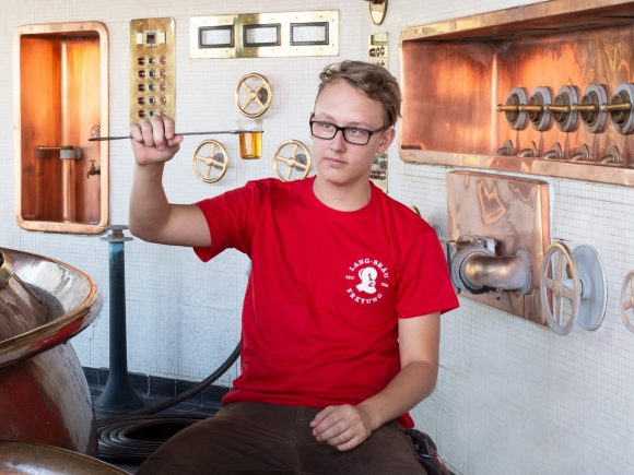 Junger Mann in rotem T-Shirt sitzt in einer Brauerei und hält ein Messgerät in der Hand.