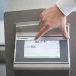 Ein Hand zeigt auf das Touchscreen-Bedienfeld eines Sesotec Geräts mit mehreren Optionen.
