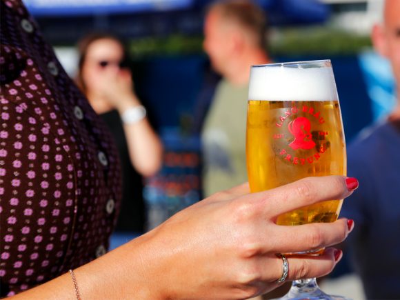 Eine Hand hält ein Glas Bier mit einem roten Logo auf der Vorderseite.