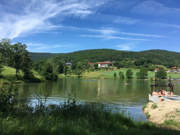 Ebenreuther See mit klarem Wasser und grünen Uferbereichen unter blauem Himmel.