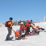 Gruppe von Skifahrern mit Handicap auf einer verschneiten Piste in den Bergen.