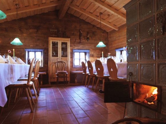 Rustikales Esszimmer mit einem langen Tisch, Stühlen und einem Holzofen in der Ecke.