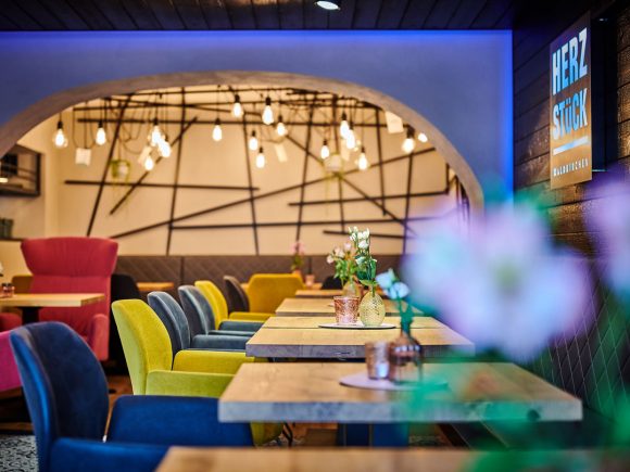 Bunte Stühle in verschiedenen Farben und Holztische in einem modernen Innenraum mit dekorativen Lampen.