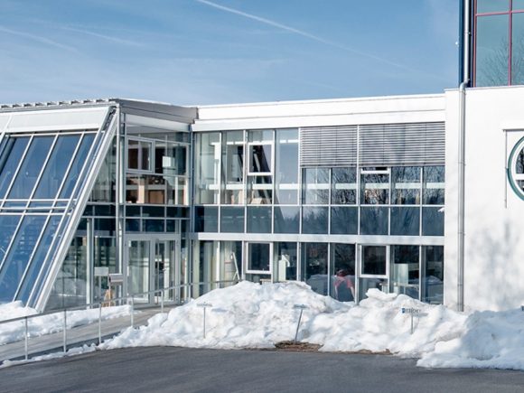 Moderne Architektur eines Unternehmensgebäudes mit großen Fenstern und einem schrägen Glasdach.