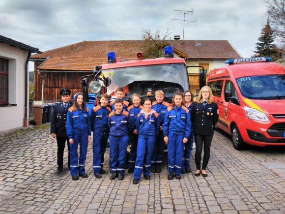 Gruppe von Jugendlichen in blauen Uniformen vor Feuerwehrfahrzeugen in einer ländlichen Umgebung.