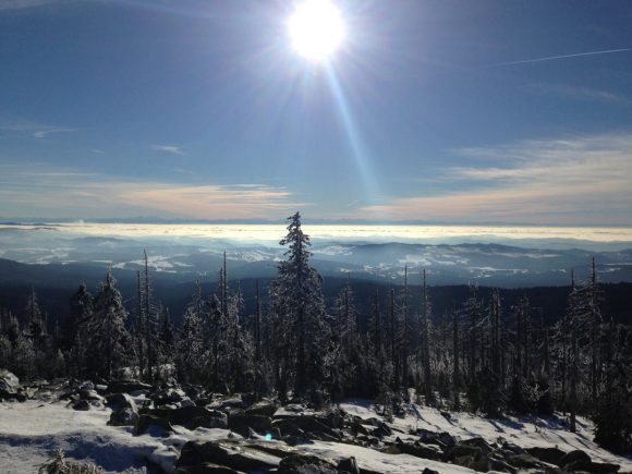 Schneebedeckte Berglandschaft mit Sonnenstrahlen und Wolken im Hintergrund.