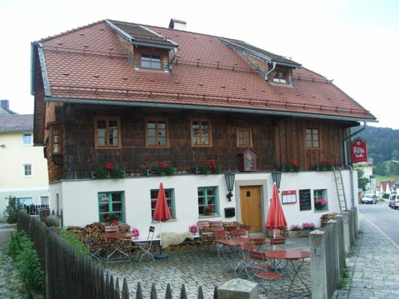 Traditionelles Gasthaus in Tirol mit Holzfassade und roten Markisen im Freien.