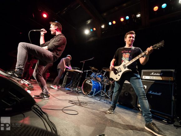 Drei Musiker einer Band, die auf einer Bühne während eines Auftritts spielen.