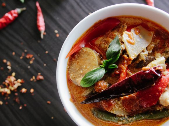 Schüssel mit thailändischem Curry, Gemüse und roten Chilischoten auf einem dunklen Hintergrund.