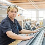 Frau mit blonden Haaren, die Materialien in einer Werkstatt bearbeitet, mit einem konzentrierten Blick.