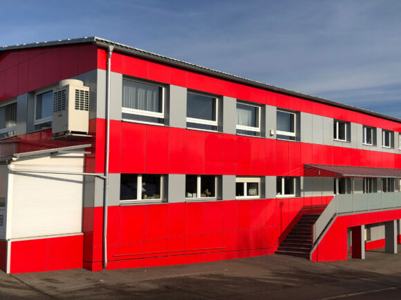 Ein rotes Gebäude mit großen Fenstern und einer Außentreppe auf der linken Seite.