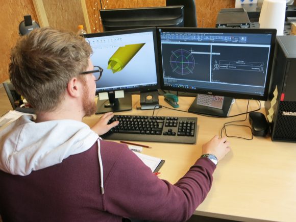Ein Mann arbeitet an einem Computer mit CAD-Software und zwei Bildschirmen in einem Büro.