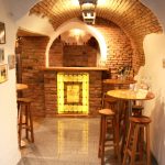 Bar mit Backsteinmauer, Holzstühlen und beleuchtetem Regal im Hintergrund.