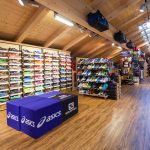 Innenansicht eines Sportgeschäfts mit Regalen voller Laufschuhe und Ausrüstung.