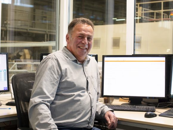 Ein Mann sitzt an einem Schreibtisch mit mehreren Computermonitoren in einem Büro.