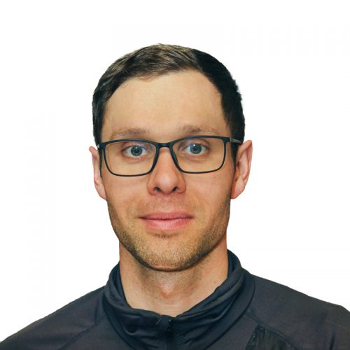 Ein Mann mit Brille und kurzem, dunklem Haar in einem schwarzen Oberteil vor einem weißen Hintergrund.