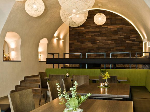 Innenansicht eines modernen Restaurants mit Holz- und Grüntönen sowie dekorativen Lampen.