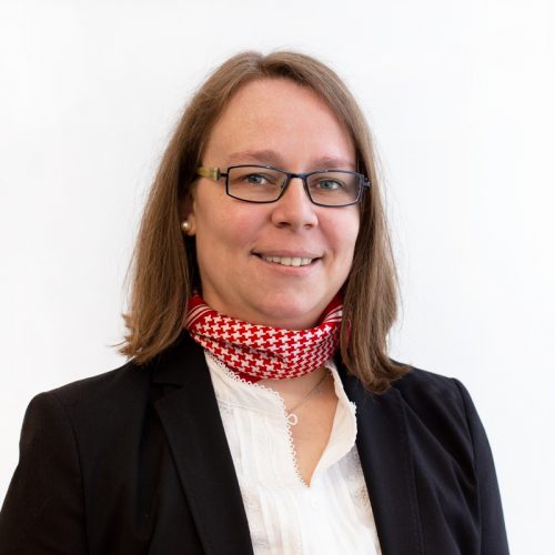 Frau mit Brille und einem roten Schal, der um den Hals getragen wird, in einem professionellen Outfit.
