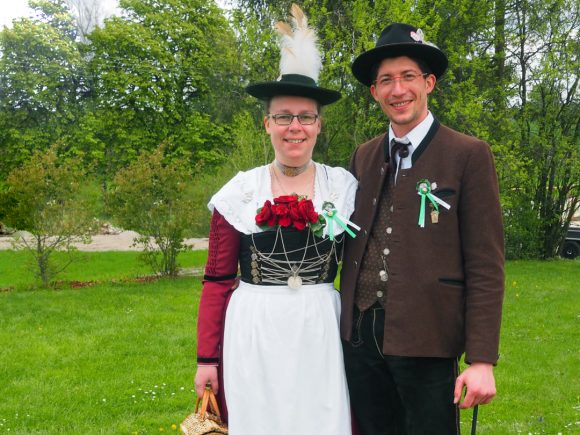 Ein Paar in traditioneller Tracht, bestehend aus einem Mann und einer Frau, beide mit Blumen und Accessoires.