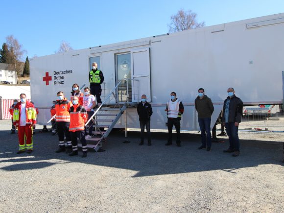 Gruppenfoto von Mitarbeitern des Deutschen Roten Kreuzes vor einer Mobilstation mit Treppe.