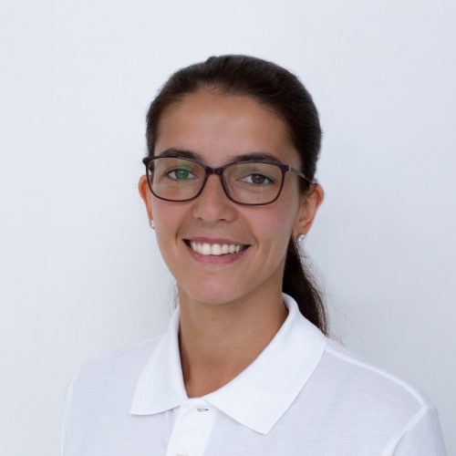 Frau mit Brille und langen Haaren, die in einem weißen Hemd lächelt.