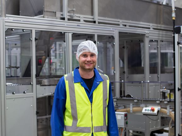 Mitarbeiter in blauer Arbeitskleidung und Sicherheitsweste in einer Produktionshalle.