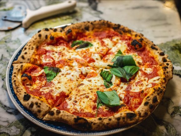 Pizza Margherita mit Tomatensauce, Mozzarella und frischem Basilikum auf einem Teller.