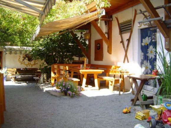 Gartenbereich mit Holztischen, Bänken und Spielzeug auf dem Boden.