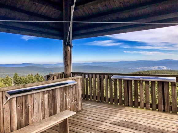Aussichtsplattform aus Holz mit Blick auf eine bewaldete Landschaft und den Himmel.