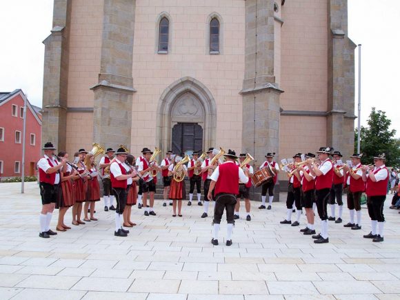 Eine Musikkapelle in traditionellen Trachten spielt vor einer Kirche in Hinterschmiding.