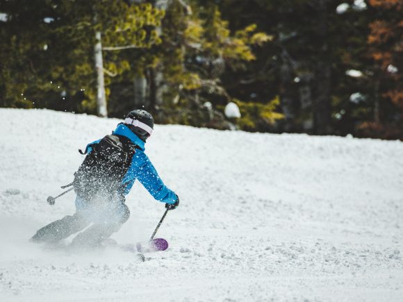 Ein Skifahrer in blauer Jacke fährt durch frischen Schnee auf einer Piste im Wald.