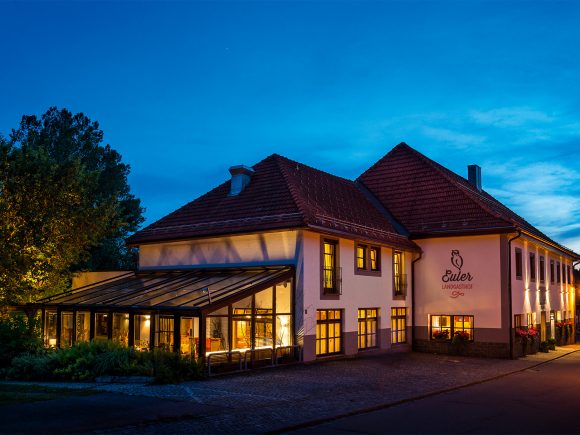 Das Gebäude des Landgasthofs Euler mit beleuchteten Fenstern und einem Glasvorbau bei Nacht.