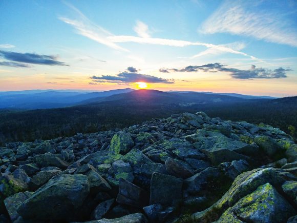 Sonnenuntergang über einer felsigen Landschaft mit Wolken und Bergen im Hintergrund.