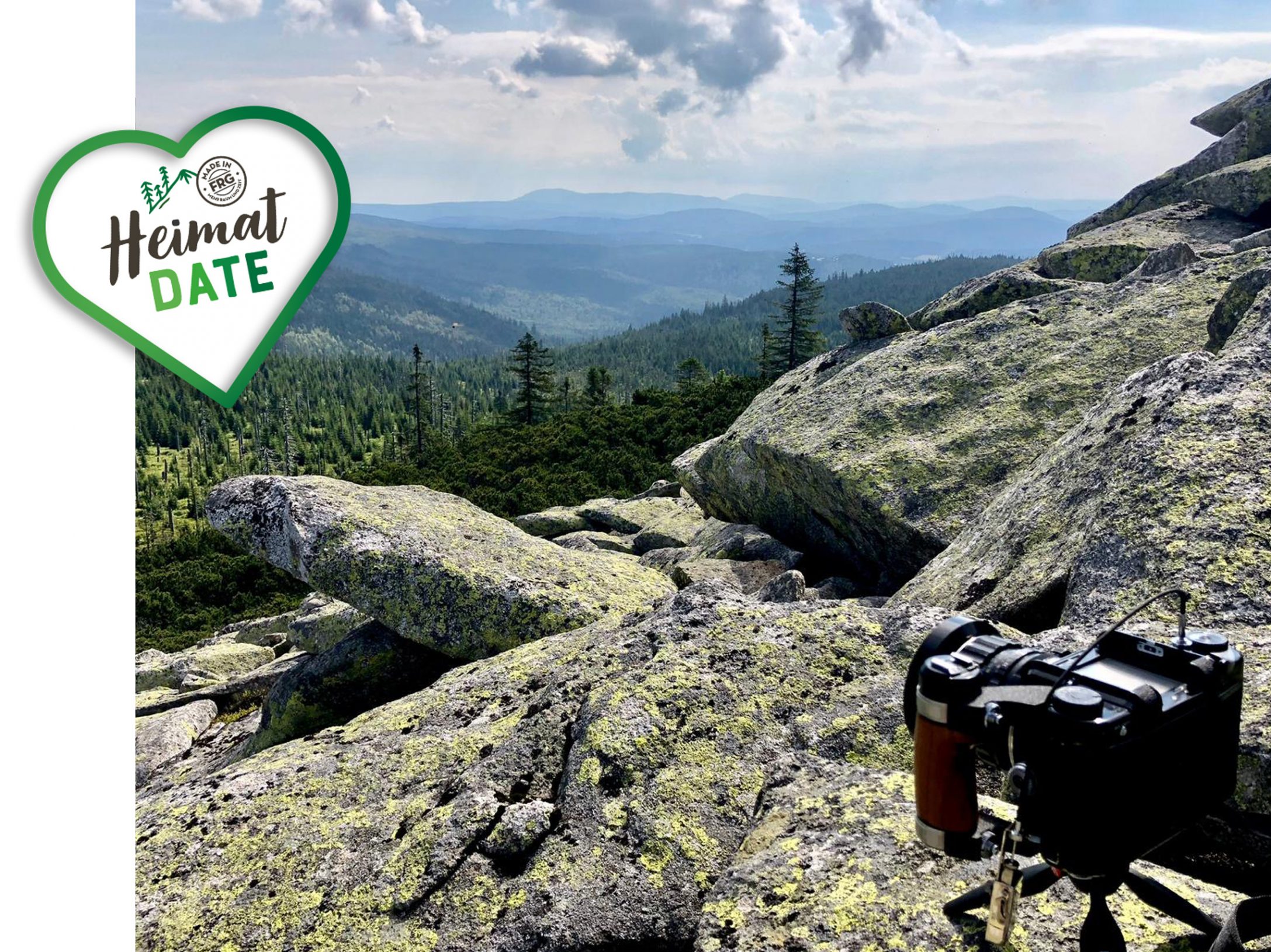 Eine Kamera auf einem Felsen mit bewaldeter Landschaft im Hintergrund und bewölktem Himmel.