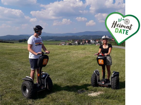 Zwei Personen fahren auf Segways in einer grünen Landschaft mit Hügeln im Hintergrund.