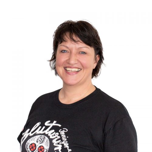 Frau mit kurzen, dunklen Haaren und einem schwarzen T-Shirt, lächelt in die Kamera.
