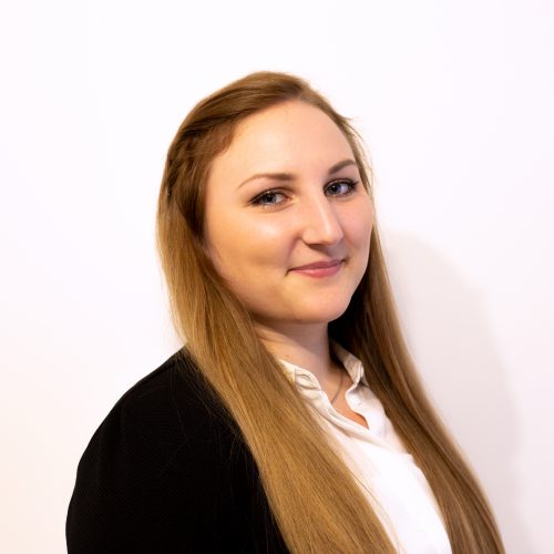 Frau mit langen, blonden Haaren und einem schwarzen Blazer, die leicht lächelt.