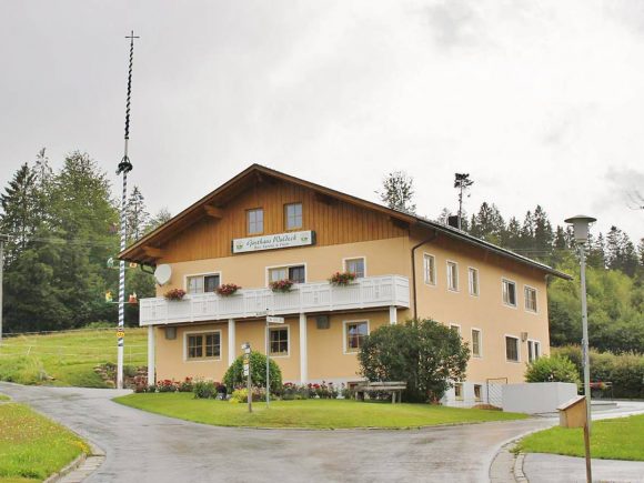 Ein Gasthaus mit gelber Fassade, Balkon und Blumen auf dem Fensterbrett in einer ländlichen Umgebung.