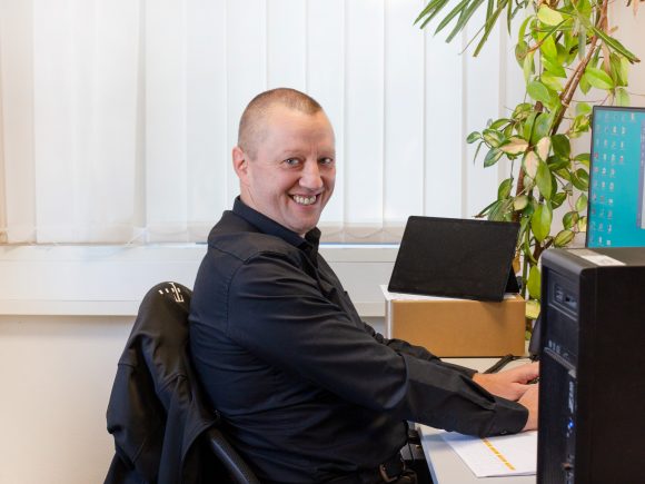 Mann mit kurzem Haar sitzt an einem Schreibtisch und arbeitet am Computer in einem Büro.