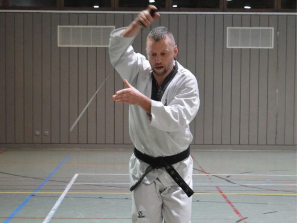 Ein Taekwondo-Praktizierender mit schwarzem Gürtel führt eine Technik in einem Trainingsraum aus.