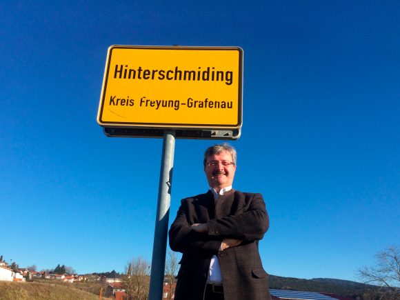 Ein Mann steht vor einem Ortsschild mit der Aufschrift 'Hinterscheidung' und 'Kreis Freyung-Grafenau'.