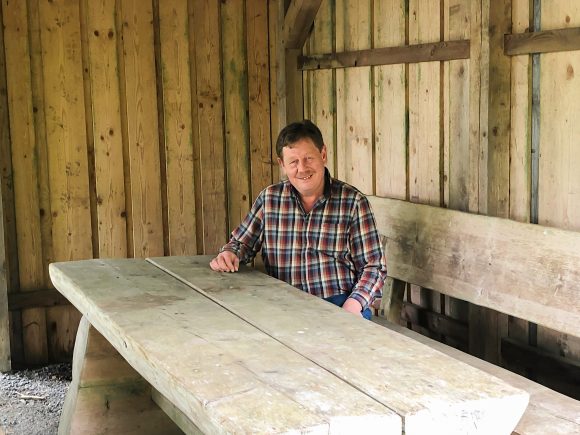 Mann sitzt an einem großen Holztisch in einer Hütte mit Holzverkleidung.